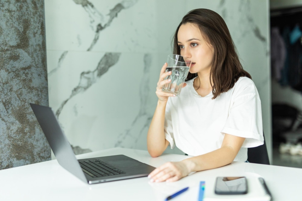 woman-drinking-from-water-glass-while-typing-her-laptop-staying-hydrated-while-working-from-home.jpg